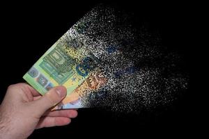 trois billets en euros tenus dans une main se décomposent et se dissolvent en raison de l'inflation avec du noir