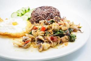 calamars sautés épicés avec feuilles de basilic et piment, œuf au miroir, servis avec riz brun. c'est la célèbre cuisine thaïlandaise. vous pouvez changer le matériel conçu et essayer de cuisiner pour votre famille.