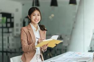 belle femme asiatique souriante travaillant au bureau, regardant la caméra. photo