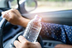 chauffeur de femme asiatique tenant une bouteille pour boire de l'eau en conduisant une voiture. une bouillotte en plastique provoque un incendie. photo