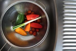 concombre tomate oignon vert et poivron dans une passoire dans l'évier de la cuisine photo