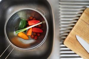 concombre tomate oignon vert et poivron dans une passoire dans l'évier de la cuisine photo