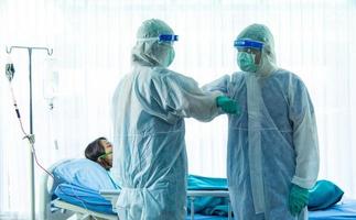 deux membres du personnel médical avec costume d'epi et masque facial debout un bras pliant à côté d'une patiente vieillissante infectée par corona visrus ou covid-19 chambre dans la salle de quarantaine de l'hôpital. photo