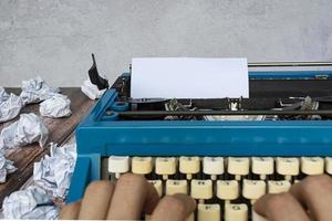 homme à la vieille machine à écrire bleue classique avec du papier poubelle sur un bureau en bois. photo