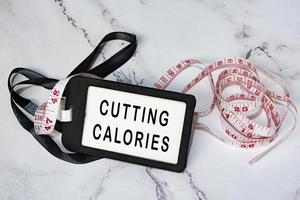 réduire les calories sur l'étiquette noire avec un robinet de mesure sur le bureau blanc. photo