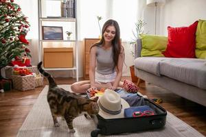 belle femme emballant des sacs pour voyager à la maison avec un chat photo