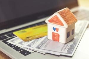 carte de crédit, modèle de maison et cahier sur un bureau en bois. achats en ligne et paiement de la maison à l'aide d'un ordinateur portable photo