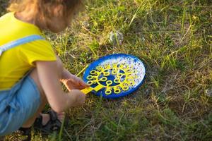 une fille en combinaison denim souffle des bulles de savon en été dans un champ au coucher du soleil. journée internationale des enfants, enfant heureux, activités de plein air. fond d'été. mode de vie sain et respectueux de l'environnement photo