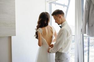 le marié aide à attacher la robe à sa mariée. photo