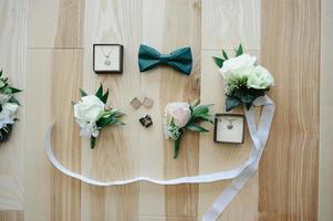 bijoux, boutonnière de mariés, boucles d'oreilles papillon et mariées sur un plancher en bois. accessoires de mariage. photo