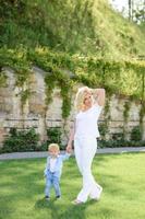 maman conduit la main de son fils à travers l'herbe verte. les deux blondes. photo