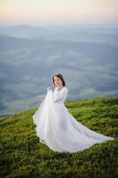 femme en robe de mariée traverse le champ vers les montagnes