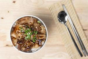 topview un bol de riz garni de poitrine de porc grillée en tranches avec de la sauce soja et des graines de sésame sur la table en bois. photo