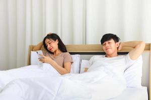 couple asiatique allongé sur le lit le matin pendant que la femme vérifie les nouvelles des médias sociaux à l'aide d'un smartphone mobile photo