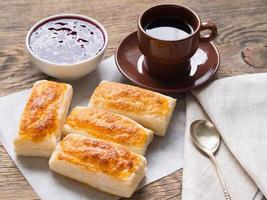 petit-déjeuner de petits pains sucrés à partir de pâte feuilletée, confiture de framboises, tasse de café sur papier parchemin. photo