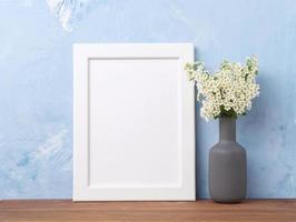 cadre blanc vierge, fleur en vaze sur une table en bois marron contre un mur de béton bleu pastel photo