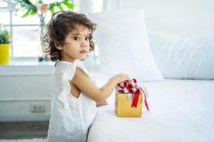 jolie petite fille heureuse après avoir reçu le coffret cadeau au lit de ses parents. en raison de l'anniversaire, joyeuses fêtes. cadeau et cadeau photo