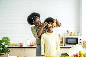 deux enfants afro-américains s'amusent et s'amusent avec des légumes alimentaires à la cuisine tient des tomates devant ses yeux comme dans des verres, enseignant à l'enfant des aliments végétariens sains et variés photo
