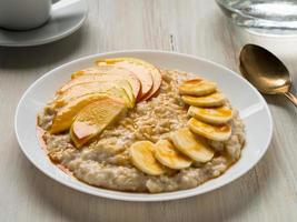 petit-déjeuner sain le matin - flocons d'avoine avec fruits et miel, tranches de pommes et de bananes, sirop de caramel. photo