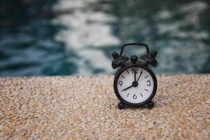 réveil noir sur sol en marbre avec fond de piscine floue. l'horloge réglée à 8 heures. photo