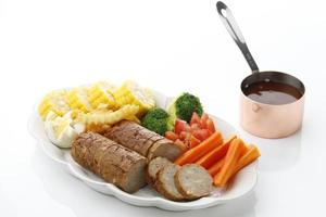 galantine de poulet, tranchée, servie sur assiette blanche avec sauce barbecue et légumes. mise au point sélective