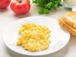 assiette blanche avec des œufs brouillés poêlés sur un fond clair blanc avec des tomates. omelette, vue de côté photo