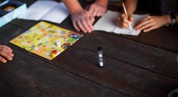 plateau de jeu de société, jetons, cube, minuterie sur une table en bois sombre et mains en arrière-plan. le concept de travail d'équipe, de détente intellectuelle, d'événement d'entreprise, de jeu à la maison avec des enfants. copie espace photo