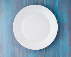 grande assiette blanche vide et plate sur une table en bois bleue, vue de dessus photo