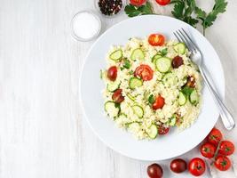 salade de légumes diététiques frais avec couscous, tomates, concombres, persil, table en bois blanc, vue de dessus, espace pour copie photo