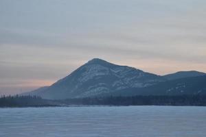 lever de soleil rose sur un sommet de montagne enneigé avec lac gelé au premier plan photo