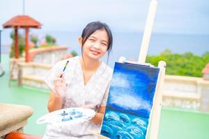 jeune fille à l'aide d'une image de dessin au pinceau sur papier de toile, à la belle vue sur le paysage à koh tao en thaïlande. photo