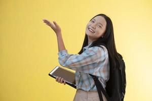 belle jeune fille avec sac à dos et tenir un ordinateur portable sur fond jaune. photo