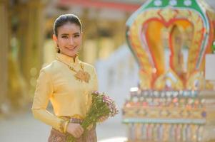jolie femme thaïlandaise dans une ancienne robe thaïlandaise tient des fleurs fraîches rendant hommage à bouddha pour faire un vœu sur le festival traditionnel de songkran en thaïlande photo