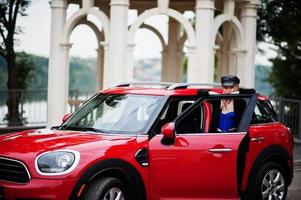 portrait d'une belle mannequin blonde sexy en casquette et en corset noir et bleu, avec un maquillage lumineux près d'une voiture de ville rouge. photo