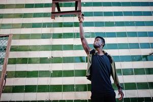 séduisant jeune homme afro-américain en vêtements décontractés debout à côté du mur carrelé. photo