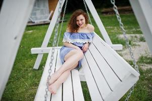 portrait d'une superbe jeune fille vêtue d'une robe bleue de style marin assise sur des balançoires au bord du lac. photo