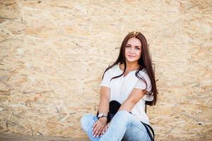 portrait d'une belle fille assise sur des planches de bois contre un mur de placage. photo