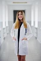 portrait d'un jeune médecin séduisant en blouse blanche avec stéthoscope posant à l'hôpital. photo