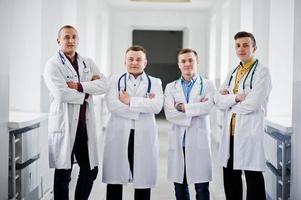 quatre médecins masculins confiants en blouse blanche avec des stéthoscopes debout dans le couloir de l'hôpital. photo