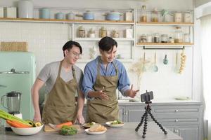 deux jeunes blogueurs amis proches préparent de la nourriture dans la cuisine tout en diffusant en direct via un smartphone.