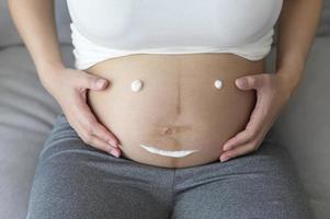 jeune femme enceinte appliquant une crème hydratante sur le ventre, les soins de santé et les soins de grossesse photo