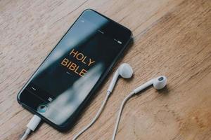 application biblique dans les téléphones intelligents sur une table en bois, lisez et écoutez la voix de dieu, symbole du concept chrétien. photo