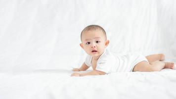 famille heureuse, mignon petit garçon nouveau-né asiatique allongé jouer sur un lit blanc regarder la caméra avec un sourire riant visage heureux. petit nouveau bébé adorable enfant innocent au premier jour de la vie. notion de fête des mères. photo