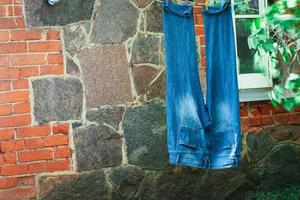 jeans bleus suspendus sur du fil pendant le séchage à l'extérieur en été sur fond de mur de brique rouge et de pierre photo