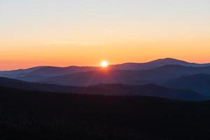 beau et lumineux lever de soleil dans les montagnes. les rayons du soleil font leur chemin depuis les sommets des montagnes brumeuses photo