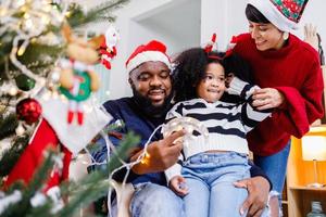la famille afro-américaine aide à décorer le sapin de noël à la maison. joyeux Noël. photo