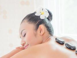 une belle femme asiatique se détend dans un magasin de spa lorsqu'une masseuse experte place une pierre chaude sur son dos photo