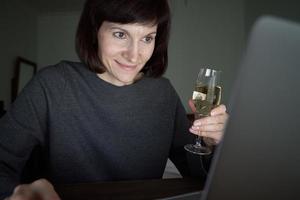 une femme parle en ligne dans un chat vidéo avec des amis et boit du vin. rencontres en ligne photo