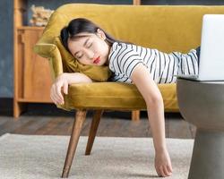 une jeune fille asiatique s'est endormie sur un canapé devant un ordinateur portable. jolie femme s'ennuie, est fatiguée ou surmenée. photo