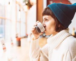 femme mature buvant du café et regardant par la fenêtre, temps froid, vêtements chauds photo